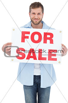 Charming young man holding a for sale sign