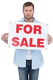 Serious young man holding a for sale sign