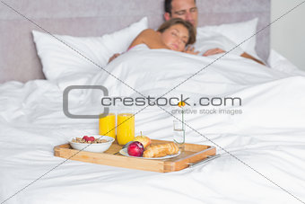 Cuddling couple asleep with breakfast tray on bed