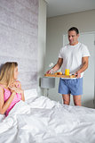 Smiling woman surprised by partner bringing breakfast in bed