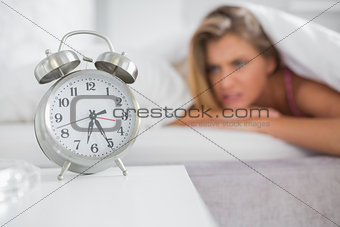 Annoyed blonde staring at her alarm clock