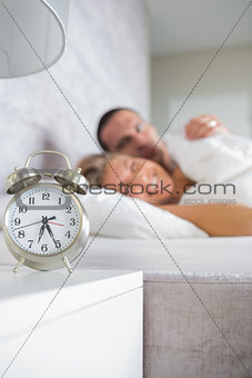 Tired couple looking at alarm clock in the morning