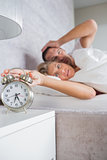 Annoyed couple looking at alarm clock in the morning with woman turning it off