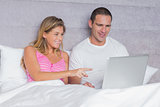 Happy young couple using their laptop together in bed