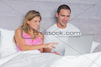 Happy young couple using their laptop together in bed