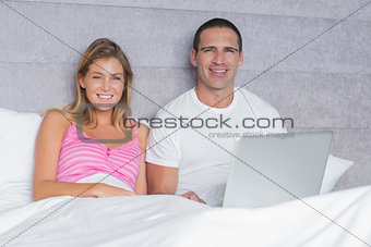 Attractive young couple using their laptop together in bed