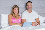 Happy young couple using their tablet pc together in bed