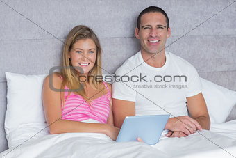 Happy young couple using their tablet pc together in bed