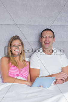 Smiling young couple using their tablet pc together in bed