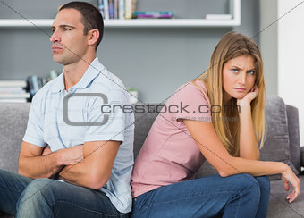 Couple sitting back to back after a fight on the couch with woman looking at camera