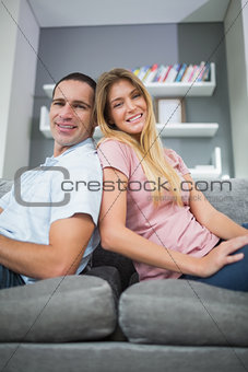 Happy couple sitting back to back on the couch together