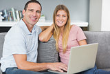Smiling couple sitting using laptop on the couch together