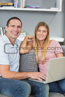 Cheerful couple sitting using laptop on the couch together