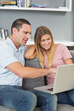 Cheerful couple sitting using laptop on the sofa together