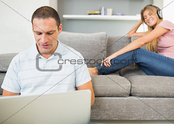 Man sitting on floor with laptop with woman listening to music on the couch