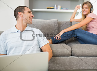 Man sitting on floor with laptop with woman listening to music on the sofa