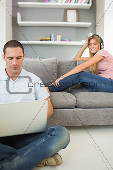 Man sitting on floor using laptop with woman listening to music on the sofa