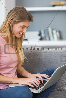 Attractive blonde sitting on her sofa using laptop