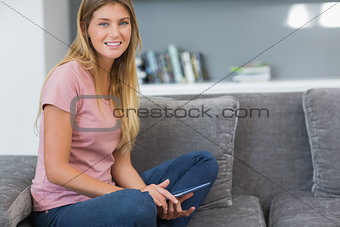 Pretty blonde sitting on her sofa using tablet pc