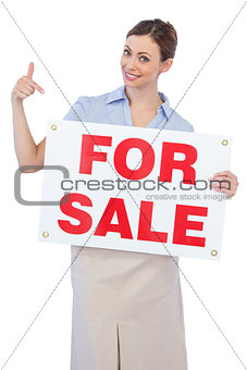 Happy estate agent posing and pointing to for sale sign