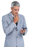 Thoughtful businessman touching his chin and looking at his phone