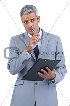 Pensive businessman holding clipboard and taking notes