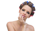 Cheerful model in hair curlers posing with hand on her face