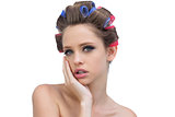 Pensive young woman in hair curlers posing and looking at camera