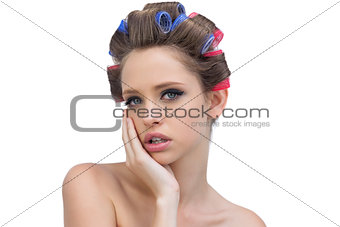 Pensive young woman in hair curlers posing and looking at camera