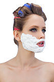 Pensive model in hair curlers with shaving foam