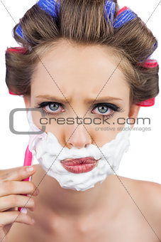 Serious model in hair curlers posing with shaving foam and razor