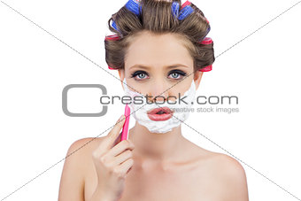Young woman in hair curlers posing with razor