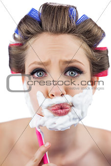 Curious model in hair curlers posing with shaving foam and razor