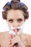 Secretive woman in hair curlers posing with shaving foam and razor