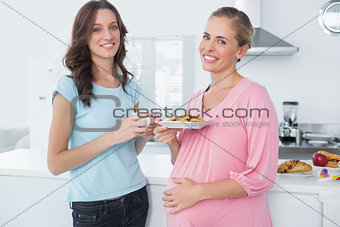 Smling pregnant woman holding cookies and her friend