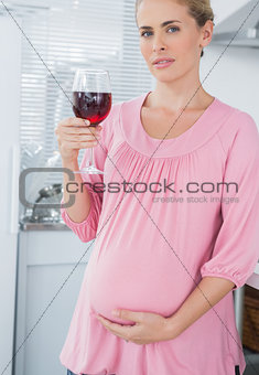 Expecting woman holding glass of red wine