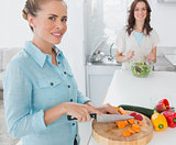 Blonde woman cutting carrots with her friend tossing salad