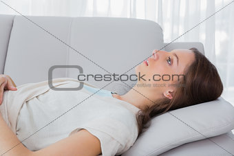 Upset brunette with a vacant look lying on the couch