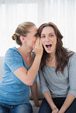 Astonished woman being told a secret by her friend