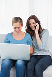 Blond woman using her laptop with her friend having a phone call