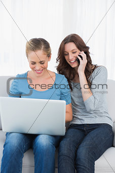 Blond woman using her laptop with her friend having a phone call