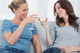 Happy women clinking their wine glasses while sitting on the sofa