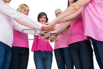 Enthusiastic women wearing pink for breast cancer posing in circle holding hands looking at camera