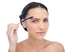 Frowning young brunette using eyebrow brush