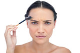 Unsmiling young brunette using eyebrow brush