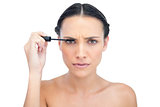 Frowning young brunette applying mascara