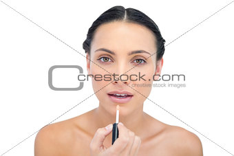 Concentrated young brunette applying lip gloss