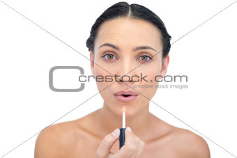Young model applying lip gloss while looking at camera