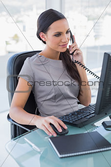 Concentrated businesswoman answering phone and working on computer