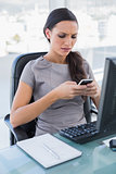 Frowning gorgeous businesswoman texting on her smartphone
